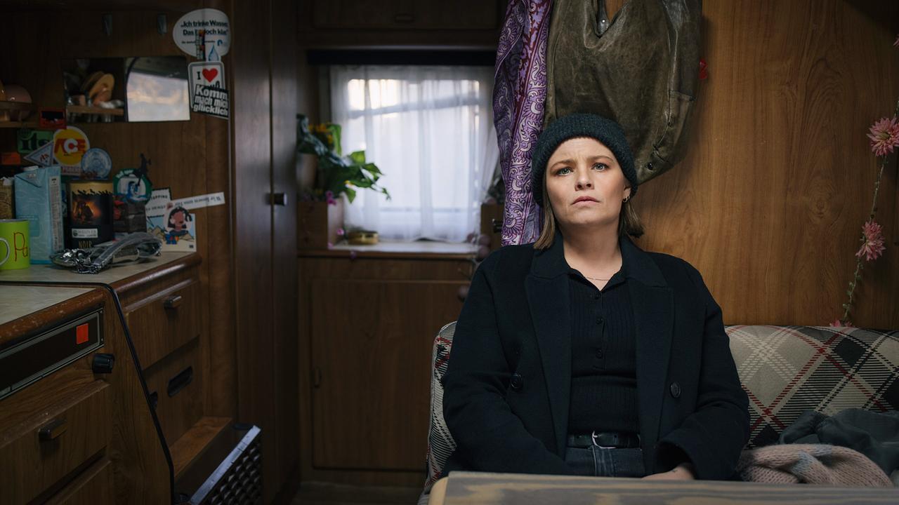 Kommissarin Liv Moormann mit Haube am Kopf sitzt in einem kleinen Wohnmobil und schaut nachdenklich nach vorne.