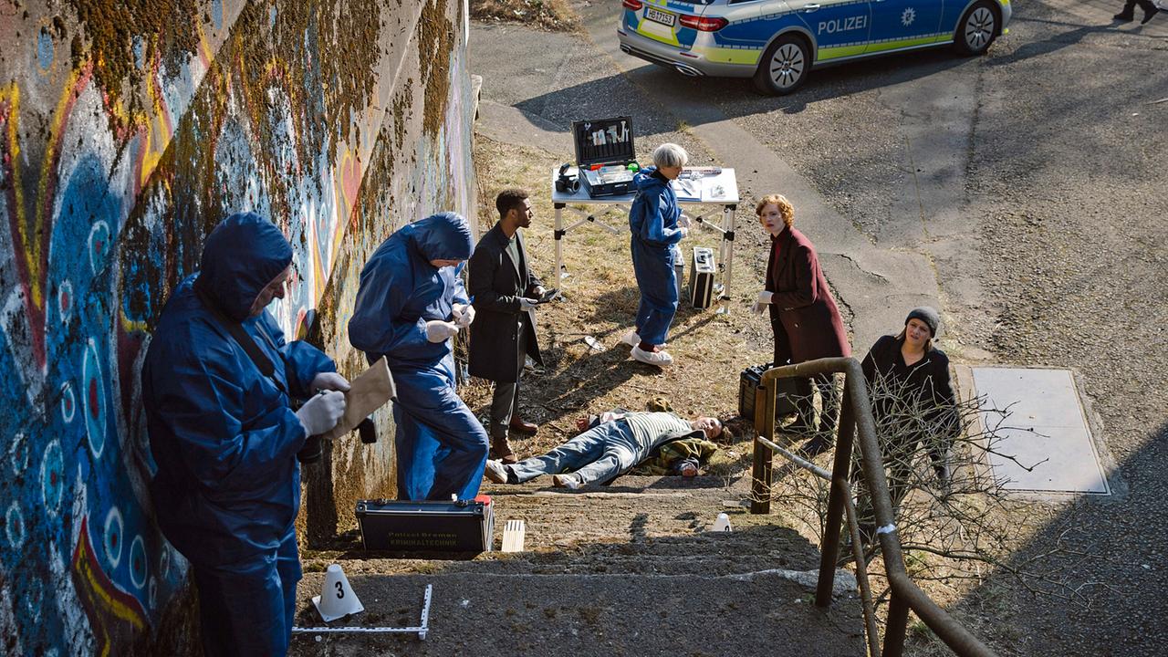 Vor dem Club „Blue Moon“ wird die Leiche einer jungen Frau gefunden: Ein Team aus Polizei und Forensikern untersucht einen leblosen Körper an einer Außentreppe.