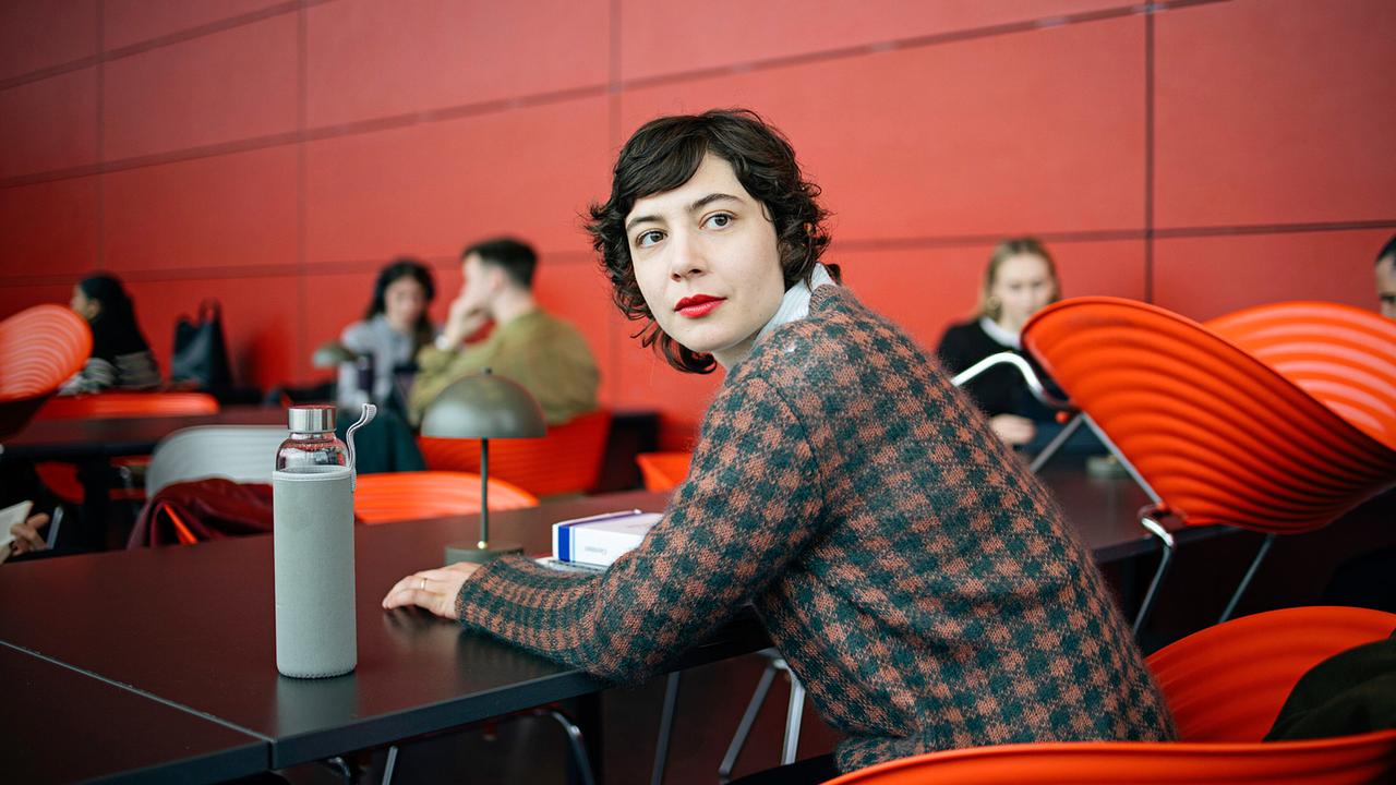 Karima Al-Sharquawi sitzt in einem modernen Raum, umgeben von anderen Studierenden.