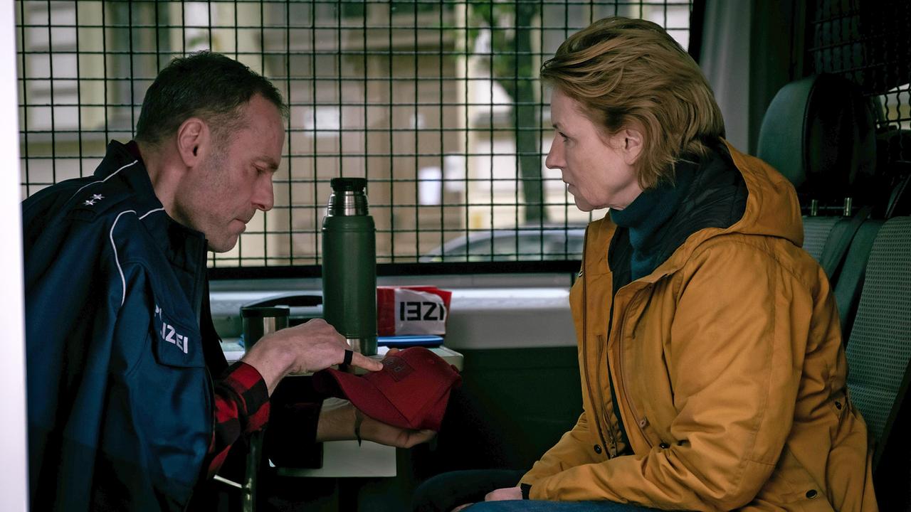 Susanne Bonard und Robert Karow, der im Gesicht verletzt ist, sitzen sich gegenüber in einem Einsatzwagen.