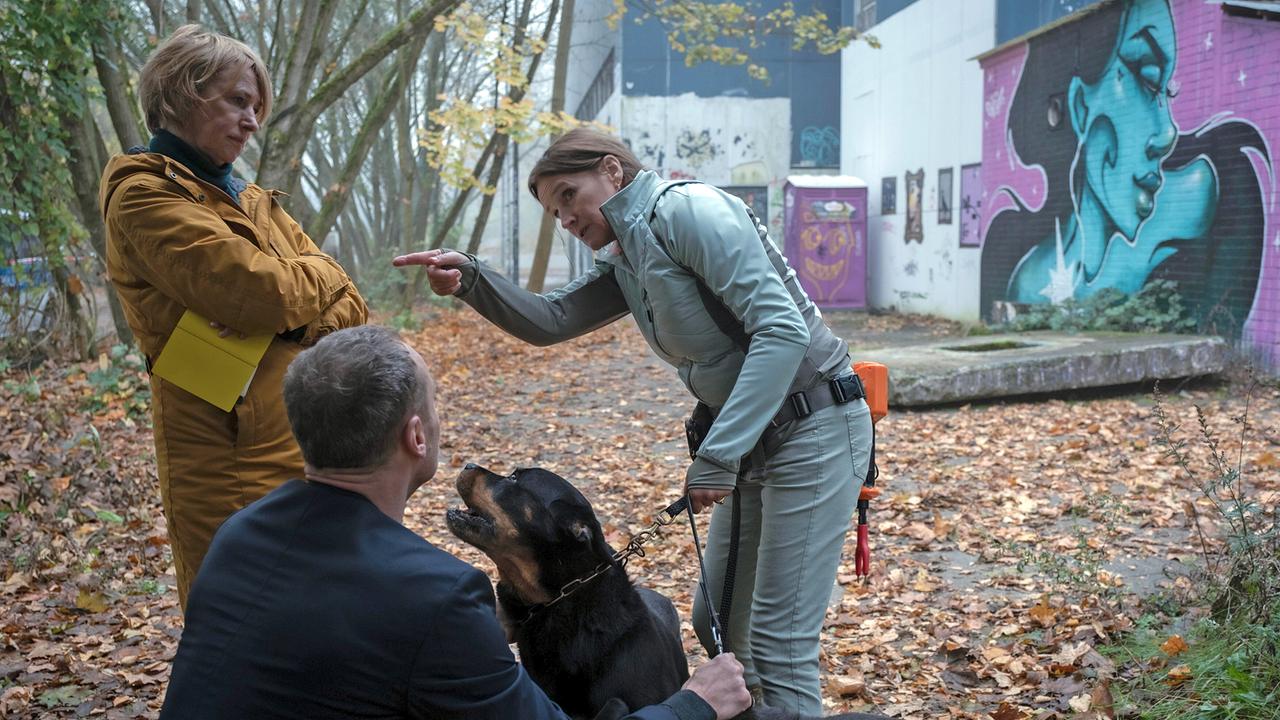 Die Spaziergängerin Edda Odin, mit einem Hund an der Leine, erzählt in der Nähe des Tatorts Susanne Bonard und Robert Karow, , wie sie den Toten gefunden hat.