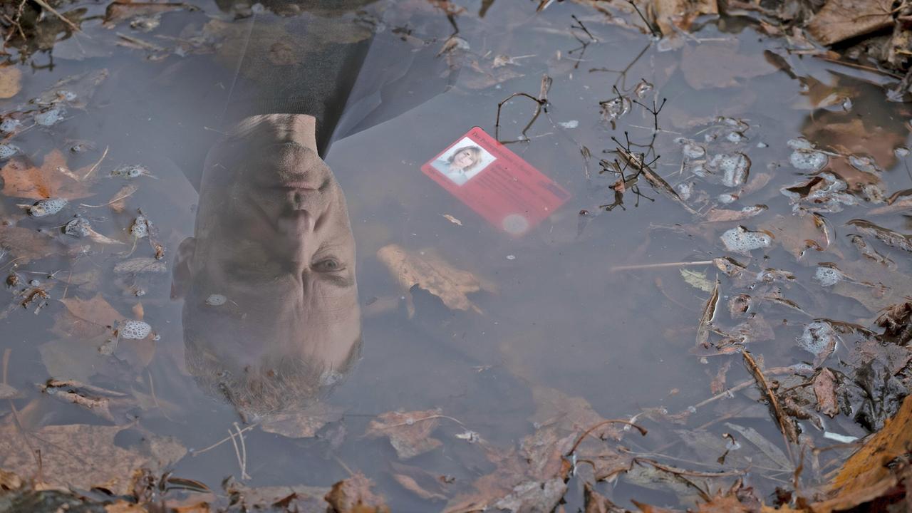 Robert Karow sieht in einer mit Blättern gefüllten Pfütze den heruntergefallenen Dienstausweis seiner Kollegin Susanne Bonard, die ihn in drei Tagen verlassen wird.