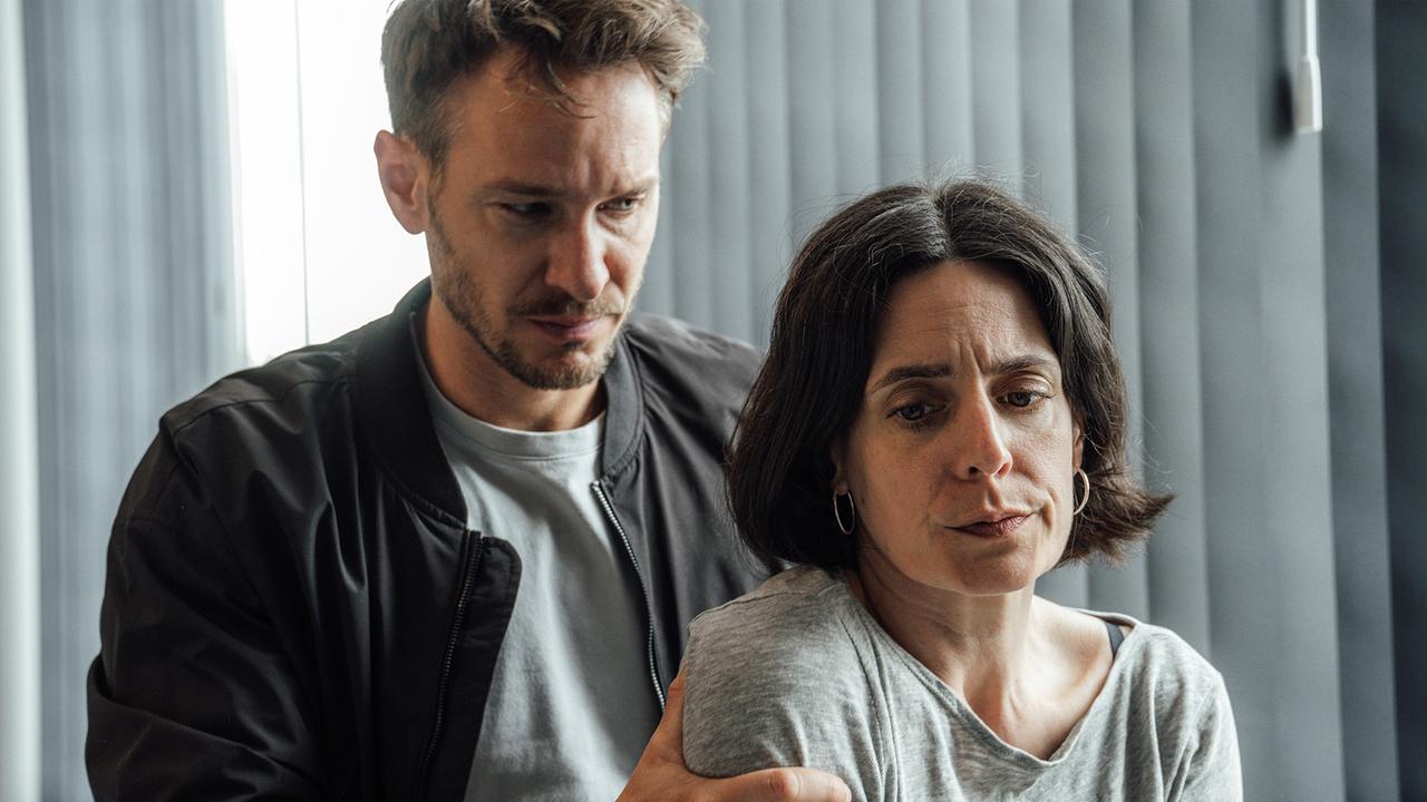 Leo Hölzer hält Esther Baumann tröstend an den Schultern in einem hellen Raum.