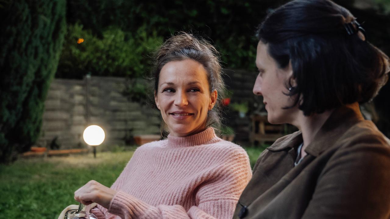 Katja Scherf und Esther Baumann sitzen abends im Garten und führen ein Gespräch bei warmem Licht.