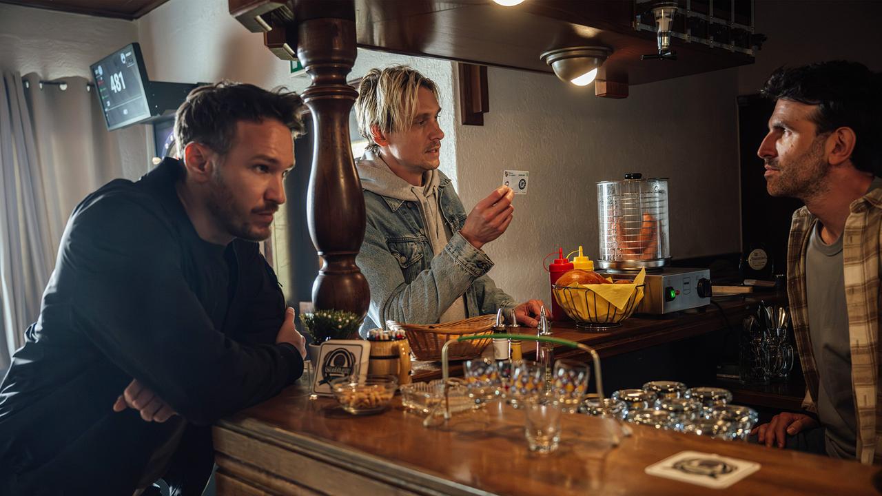 Die Kommissare Leo Hölzer und Adam Schürk befragen den Wirt Clemens Scherf an der Bar, während Adam Schürk eine Karte zeigt.