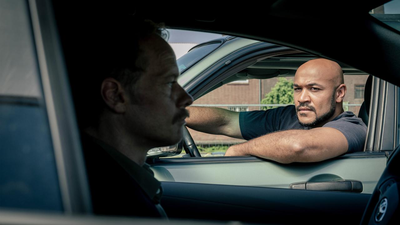 Otto Pösken und Daniel Kossik unterhalten sich durch die Autofenster zweier nebeneinander stehender Autos.