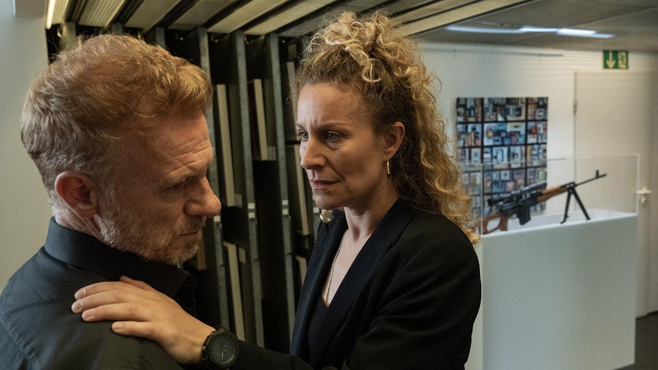 In einem Raum mit Ausstellungsvitrinen legt Ira Klasnić Lorik Duka die Hände auf die Schultern und redet ihm ins Gewissen, im Hintergrund sind Waffen ausgestellt.