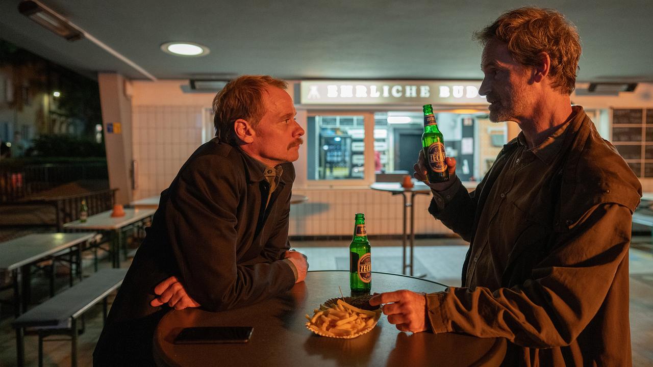 Daniel Kossik und Peter Faber unterhalten sich bei einer Currywurst über die Ermittlungen zum Mord an Haller in gewohnt feindseliger Manier.