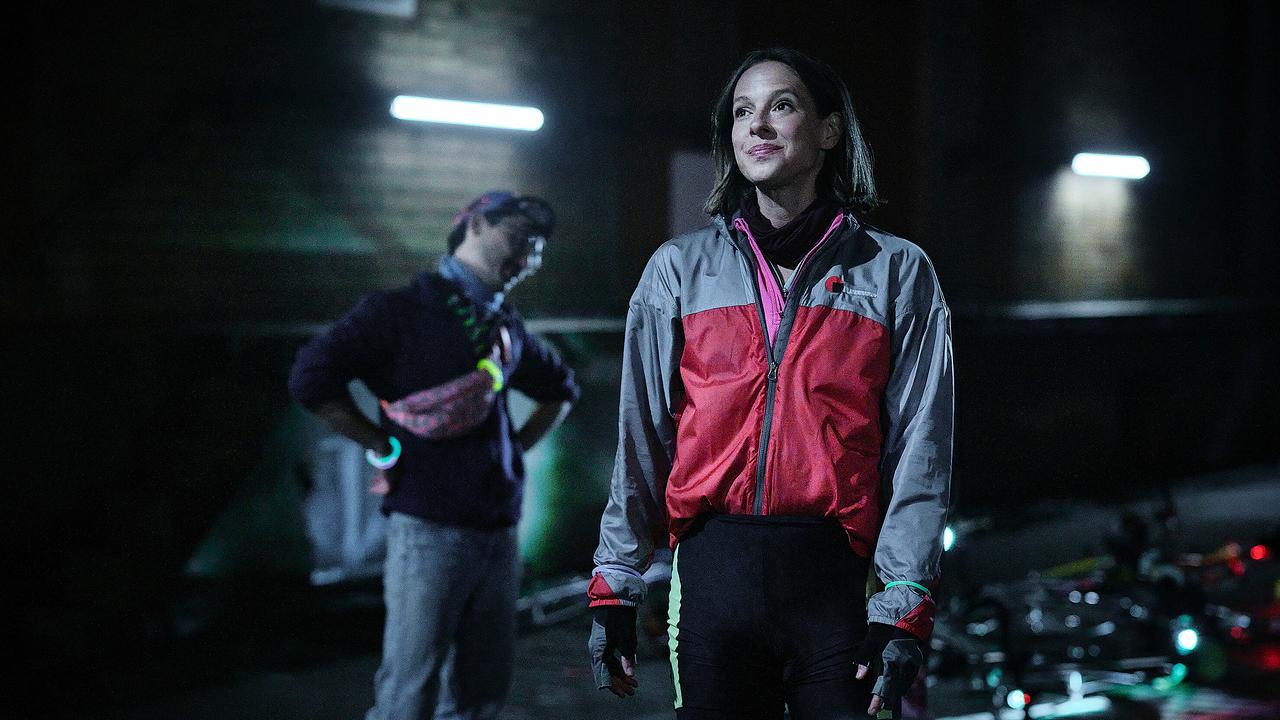 Johanna Stern in Sportbekleidung und ein weiterer Fahrradkurier stehen nachts in einer dunklen, urbanen Umgebung.