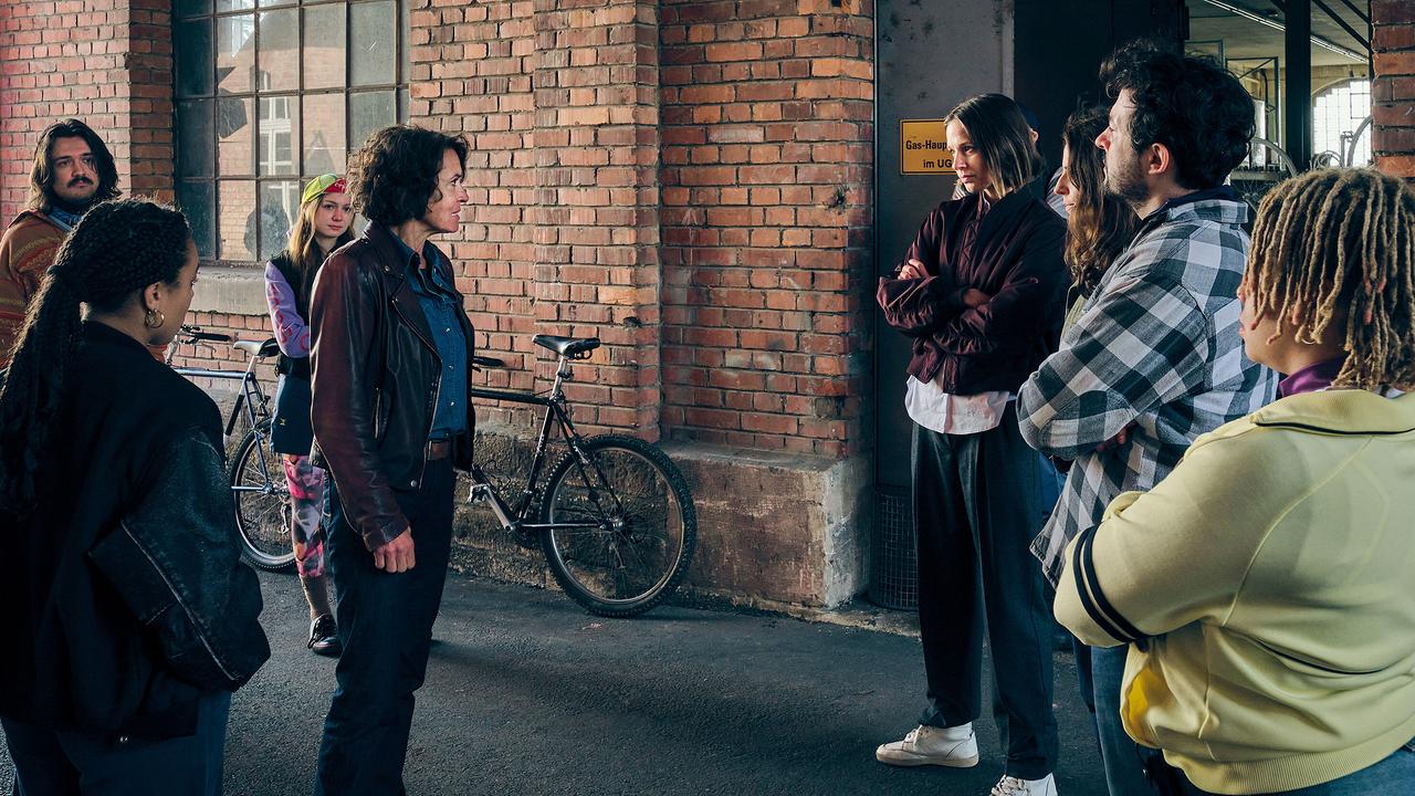 Die Velopunks mit Johanna Stern stehen wenig begeistert um Lena Odentha herum vor einem alten Backsteingebäude. 