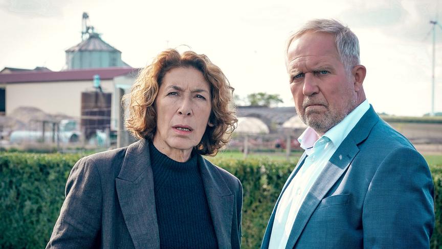 Bibi Fellner und Moritz Eisner stehen vor einem landwirtschaftlichen Betrieb und blicken nach vorne.