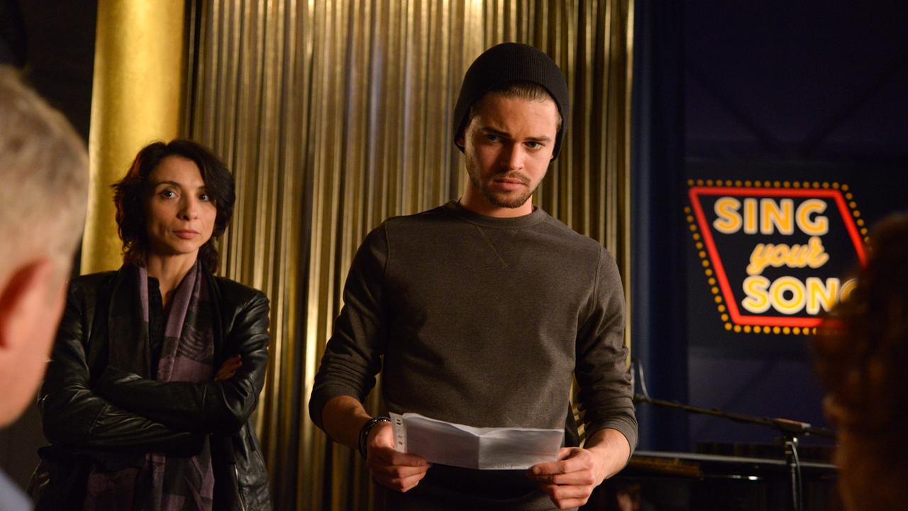 © ORF/Hubert Mican In einer Proberaumszene von "Sing your Song" steht Aris Graf mit einem Notenblatt in der Hand, während Samy Graf daneben steht und die Profile von Moritz Eisner und Bibi Fellner im Vordergrund zu sehen sind.