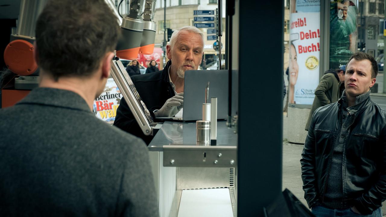 "Tatort: Tiere der Großstadt": Entwickler Klaas Andresen (Frank Leo Schröder) erklärt am Tatort Mark Steinke (Tim Kalkhof) und Karow (Mark Waschke) den Roboter, der Kaffee ausschenken kann.
