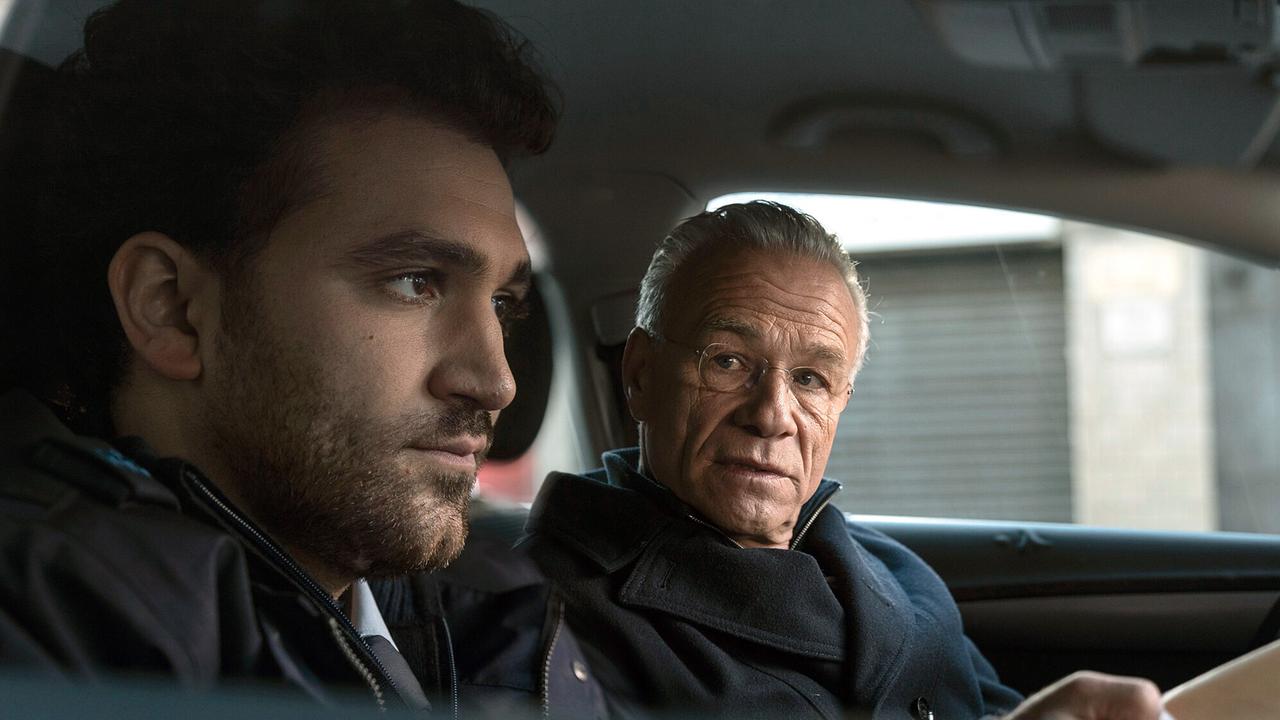 "Tatort: Vier Jahre": Polizist Emre Topal (David Vormweg) und sein Kollege versuchten für Ruhe zu sorgen auf der Silvesterparty vor vier Jahren. Dass Kommissar Max Ballauf (Klaus J. Behrendt, r) ihn jetzt ausgerechnet zu diesem Einsatz nochmal befragt, kommt überraschend. Aber er versucht sich zu erinnern – so gut es eben geht nach all der Zeit.