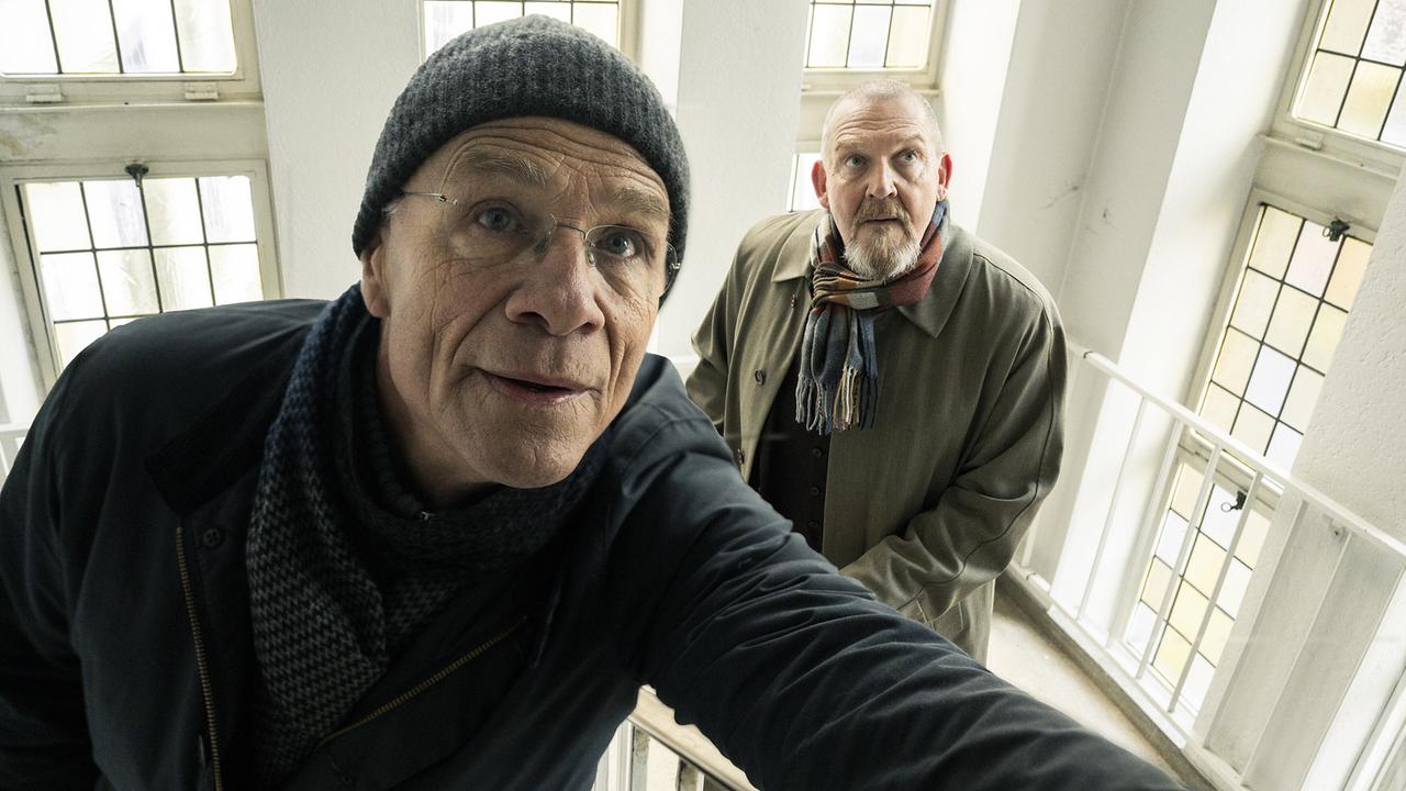 Gefahr im Verzug: die Kommissare Max Ballauf und Freddy Schenk sind im Einsatz und befinden sich in einem hellen Treppenhaus und blicken nach oben..