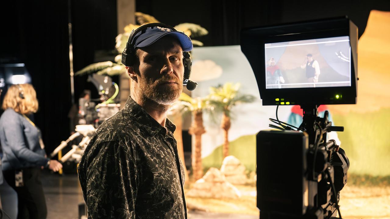 Der Kameramann Stefan Glück mit Headset steht vor einer laufenden Kamera mit Monitor auf einem Filmset. Er gehört von Anfang an zum Team der legendären Kindershow "Sachen und Machen".