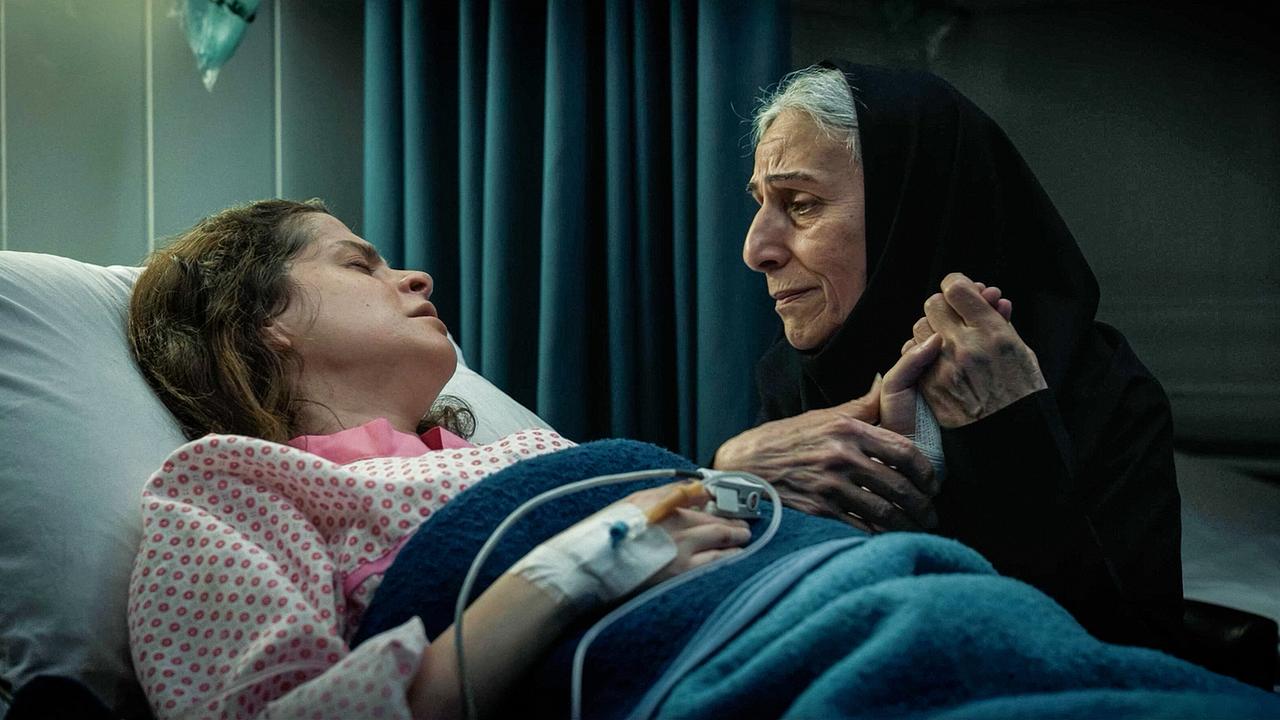 Die ältere Tarlan in schwarzem Kopftuch hält am Krankenbett die Hand der jungen Patientin Ghazal.