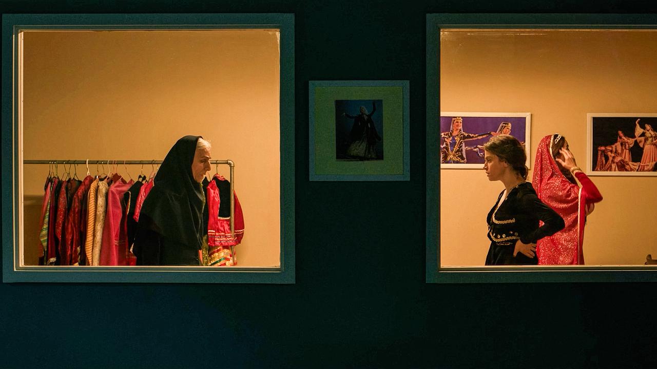 In einem Garderobenbereich steht Tarlan mit Ghazal und einer weiteren Frau in traditionellen, farbenprächtigen Kostümen.