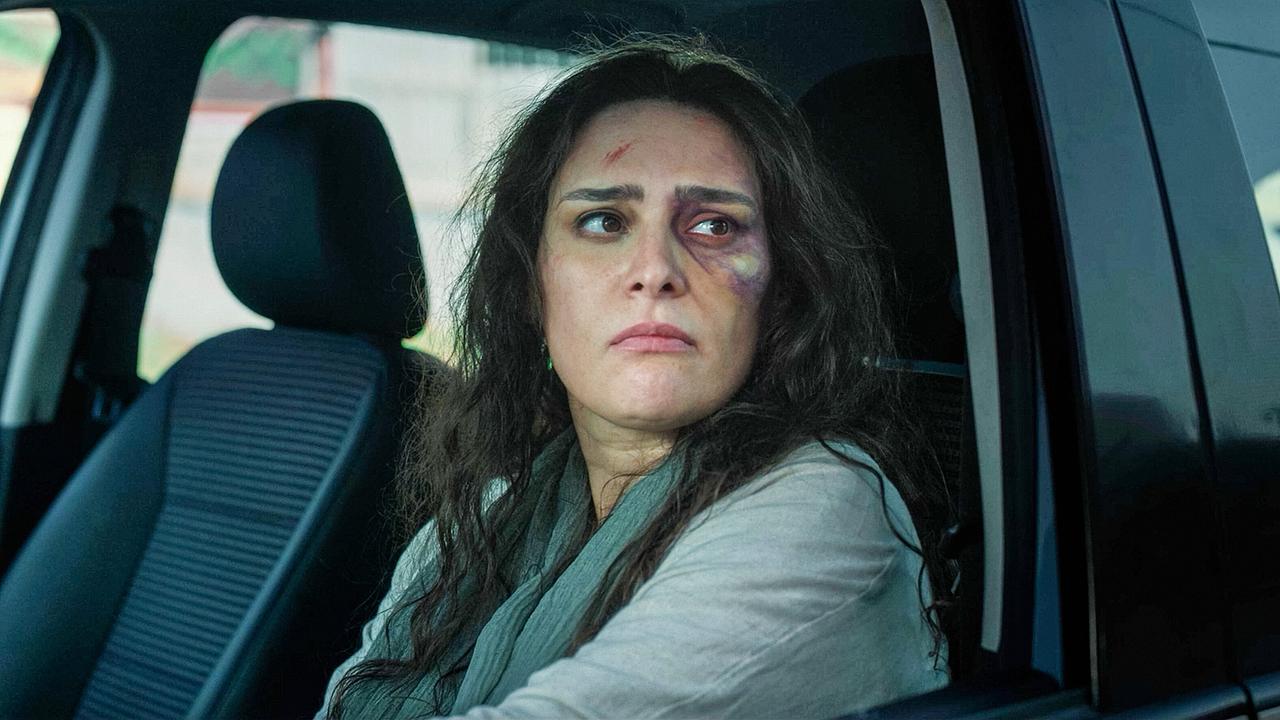 Zara mit sichtbaren Verletzungen im Gesicht sitzt angespannt am Steuer eines Autos.