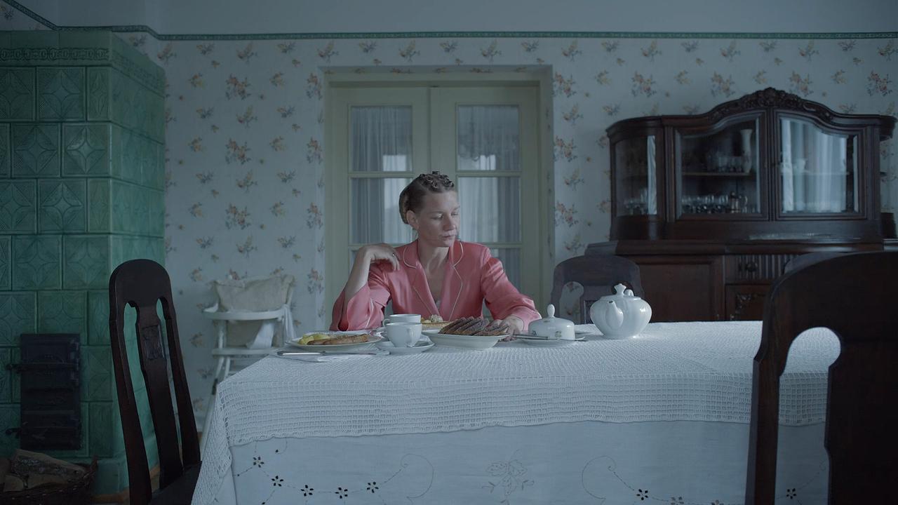 Sandra Hüller sitzt als Hedwig Höß im Wohnzimmer am Tisch, auf dem Teekannen und Teegeschirr stehen