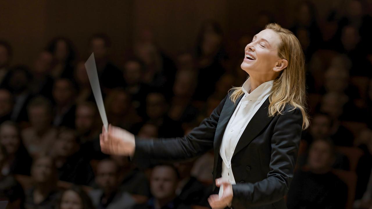 © ORF/Universal/Focus Features Cate Blanchett als Lydia Tár im Frack am Dirigentenpult, von der Musik mitgerissen lächelt sie mit geschlossenen Augen und schwingt den Taktstock, im Hintergrund Publikum im abgedunkelten Zuschauerraum
