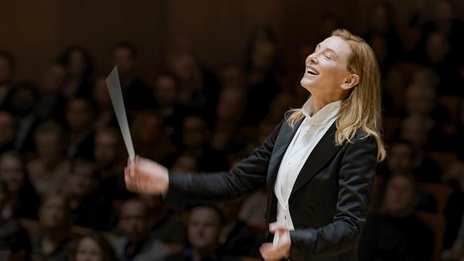 Cate Blanchett als Lydia Tár im Frack am Dirigentenpult, von der Musik mitgerissen lächelt sie mit geschlossenen Augen und schwingt den Taktstock, im Hintergrund Publikum im abgedunkelten Zuschauerraum