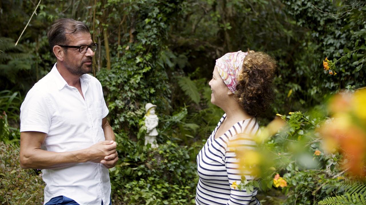 Reine Claude Gonthier und Karl Ploberger im Gespräch im Garten des Piton Betoum, umgeben von üppigem Grün und Blumen