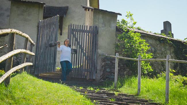 Johanna Reiter geht aus einem Holztor der Kirchenmauer von St. Benedikten, eine Steintreppe im Grünen hinab.