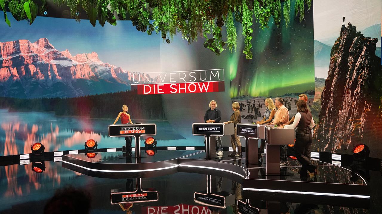 Mirjam Weichselbraun, Gregor Seberg, Nicola Feichtegger, Maria Angelini-Santner, Harald Zeitlhofer, Hans Knaus Julia Lauss stehen an ihren Pulten im farbenfrohen Studio von „Universum – Die Show“.