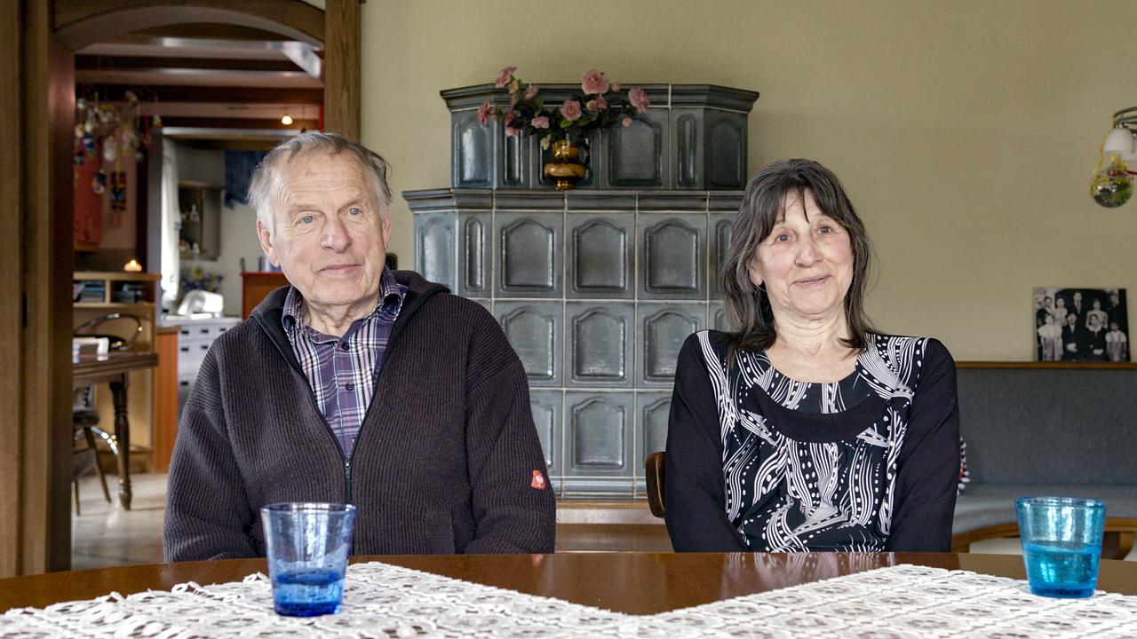 Tomi und Antonia Sabotnik sitzen an einem Esstisch in einem gemütlichen Zuhause mit Kachelofen im Hintergrund.