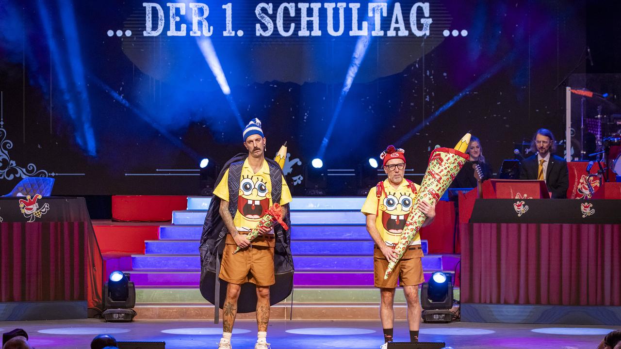 © ORF/Peter Krivograd Thomas Springer und Hans-Jörg Petrik in SpongeBob‑Kostümen stehen unter dem Schriftzug „…DER 1. SCHULTAG…“ und halten Schultüten.