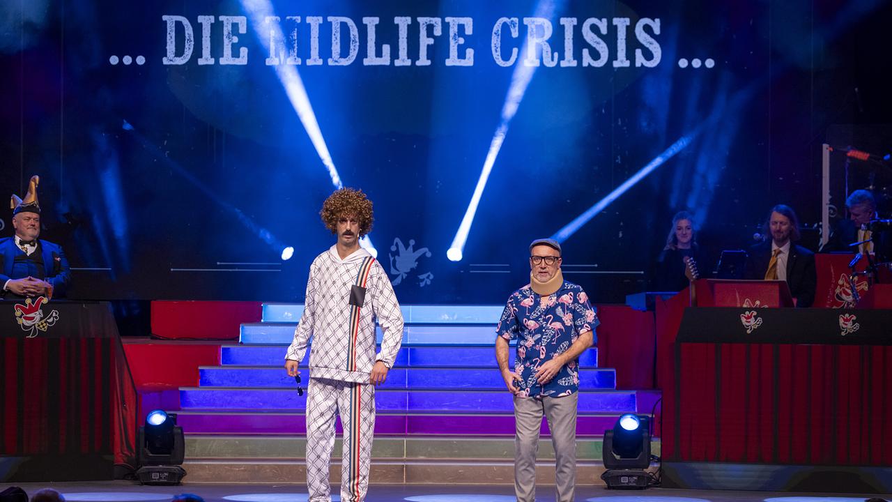 © ORF/Peter Krivograd Thomas Springer und Hans-Jörg Petrik stehen unter dem Schriftzug „…DIE MIDLIFE CRISIS…“ in lässigen Outfits auf der Showbühne.