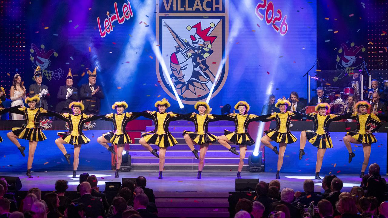 © ORF/Peter Krivograd Die "Villacher Fasching" in gelb‑schwarzen Kostümen tanzt in einer Reihe synchron vor dem Villach‑Wappen und dem Schriftzug „Lei‑Lei 2026“.