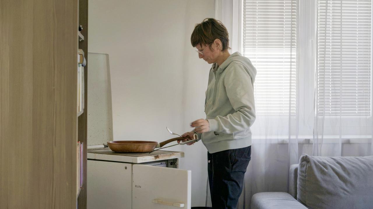 © ORF/Red Monster Film Lisa Kröbmannsberger, alleinerziehende Mutter, kocht in einem Wohnzimmer, in dem auch ein Herd zwischen einer Coach und einem Regal steht.