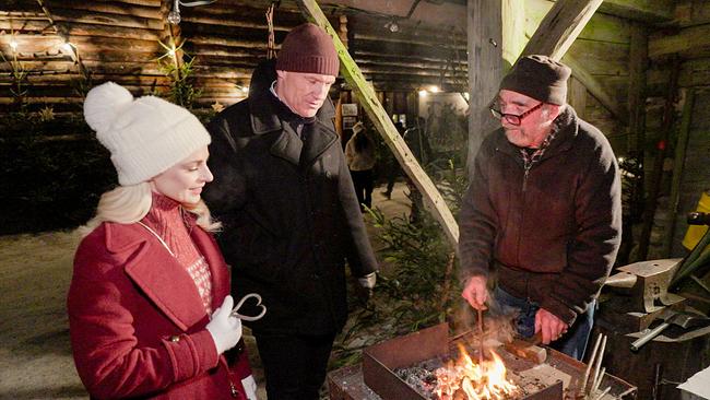 Silvia Schneider und Armin Assinger stehen bei Hans Rohringer, der an einer Feuerstelle arbeitet.