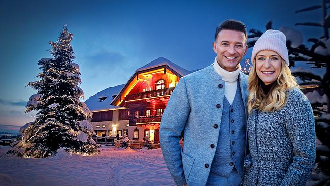 Marco Ventre und Stefanie Hertel  posieren winterlich gekleidet vor dem stimmungsvoll beleuchteten Gut Aiderbichl im Schnee. 