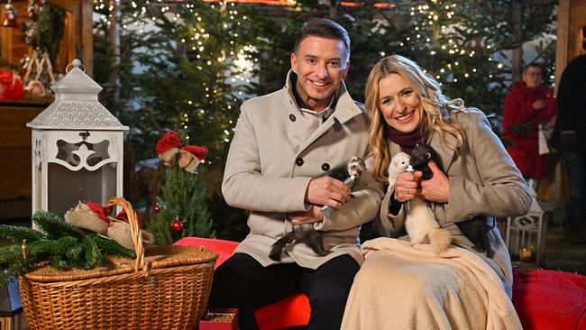 Marco Ventre und Stefanie Hertel in winterlicher Kleidung sitzen auf einer Bank vor Weihnachtsbäumen und kleine Tiere auf dem Schoß.