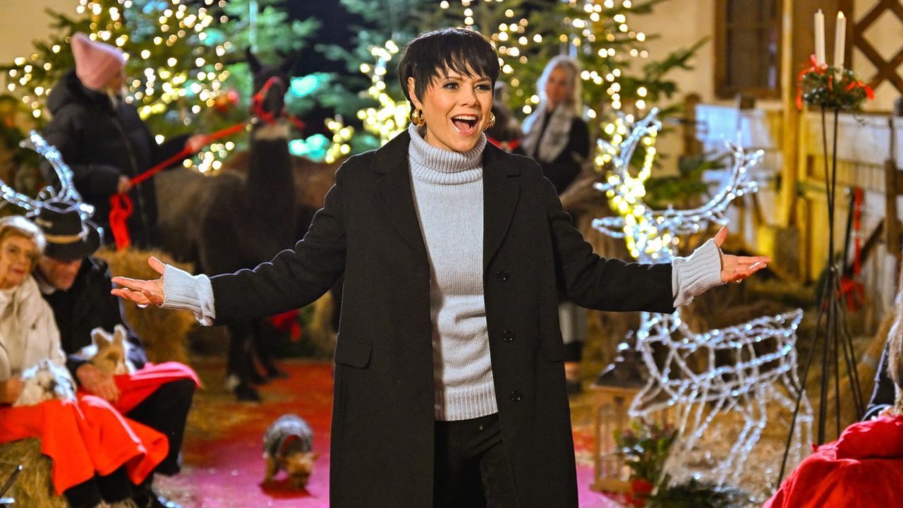 Francine Jordi singt mit offenen Armen auf einem roten Teppich inmitten von Weihnachtsbäumen, Lichterketten und Tieren.