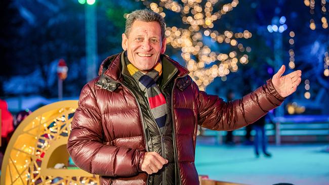 Franz Posch mit Schal und braunem Anorak steht abends lächelnd vor einem beleuchteten Eislaufplatz 
