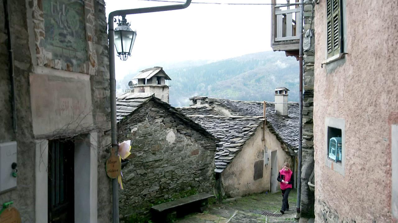 © ORF/Spiegel TV / M. Pappalardo / A. Leonardi Das pittoreske Bergdorf Monteviasco mit steinernen Häusern, Schieferdächern und Letizia Rubinato, die bergauf durch das Dorf geht.