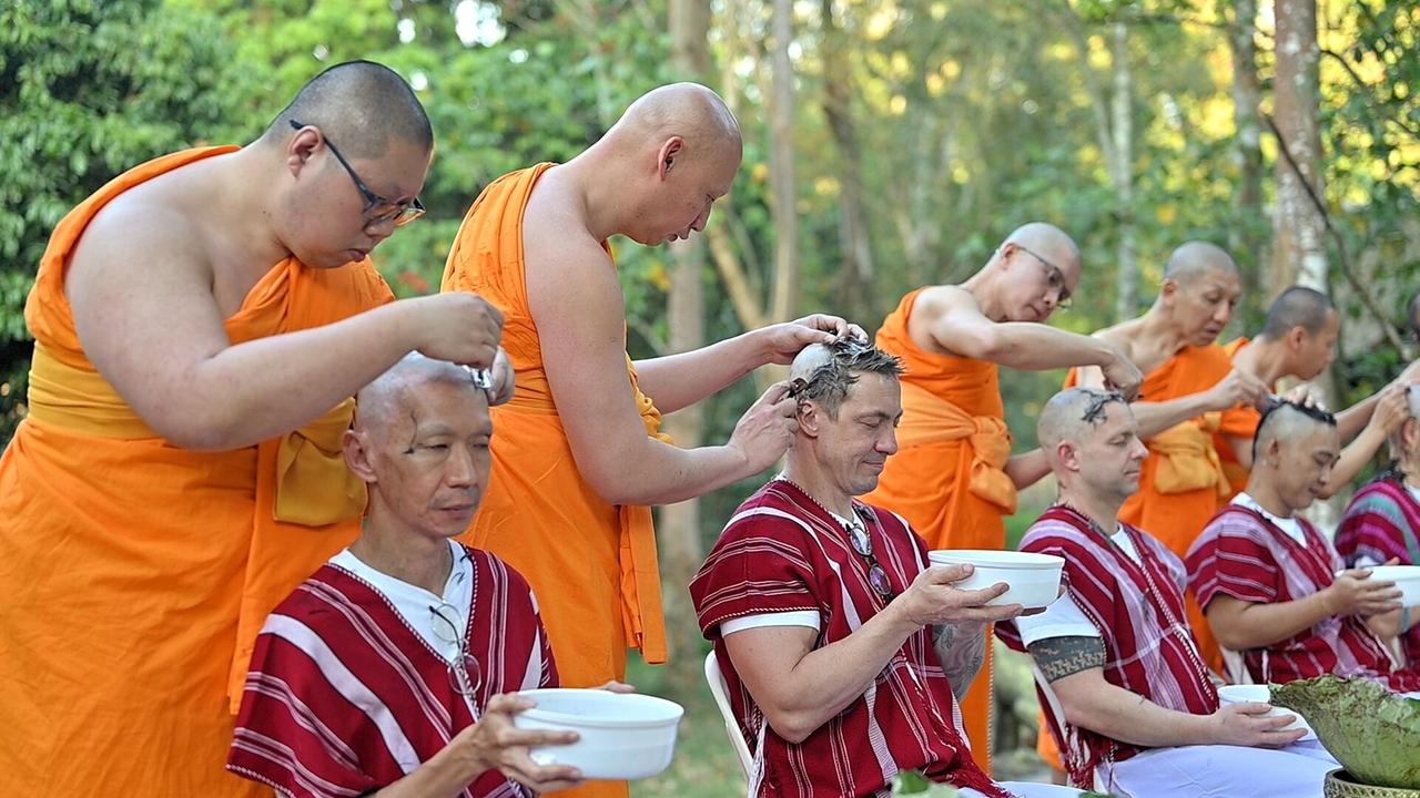 © ORF Bei der zeremonielle Kopfrasur rasieren thailändische Mönche in orangener Kutte im Grünen sitzenden Männern den Kopf. Diese dürfen im Anschluss die orangene Mönchskutte tragen.