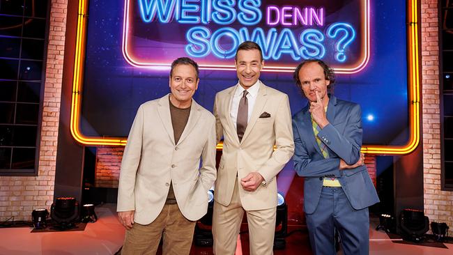 Dieter Nuhr, Kai Pflaume und Olaf Schubert stehen im TV-Studio vor einem leuchtenden Neon‑Logo mit der Aufschrift "Wer weiß denn sowas?"