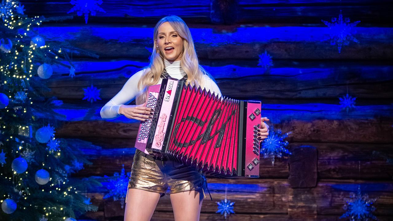 Melissa Naschenweng  spielt auf einer pinken Steirischen Harmonika auf einer weihnachtlich-dekorierten Holzbühne vor einem festlich geschmückten Weihnachtsbaum.