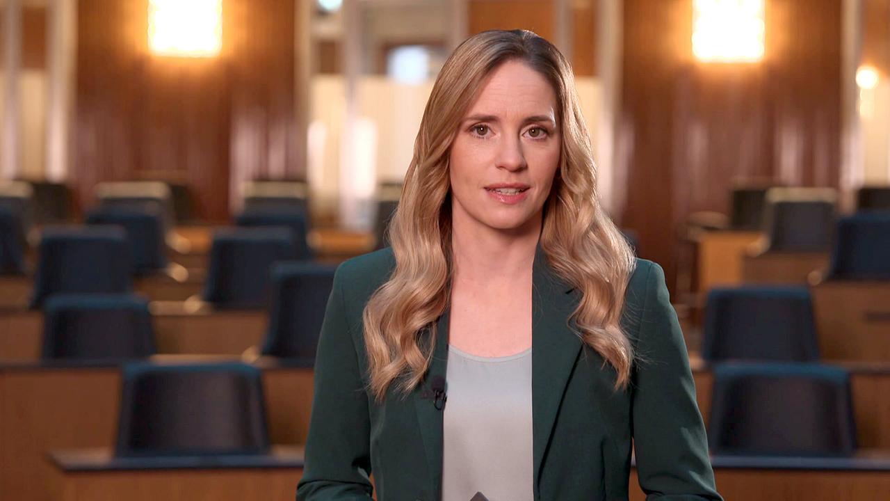 Margit Laufer steht frontal in einem leeren parlamentarischen Plenarsaal