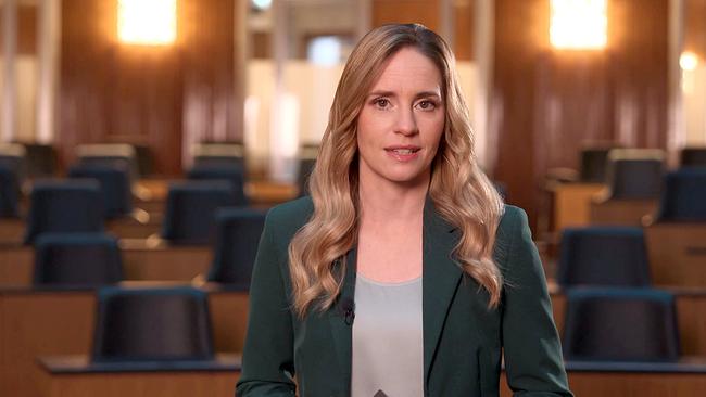 Margit Laufer steht frontal in einem leeren parlamentarischen Plenarsaal