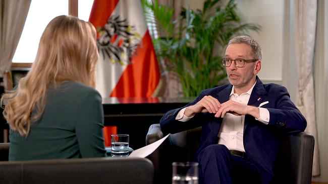 Margit Laufer im Gespräch mit FPÖ Parteichef Herbert Kickl in einem Raum mit einer österreichische Flagge und Zimmerpflanzen im Hintergrund.