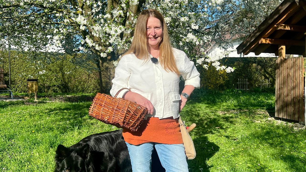 Monika Vesely steht mit einem Korb vor einem blühendem Baum in ihrem Garten.