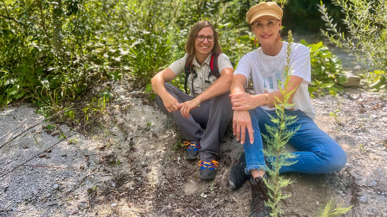 Maggie Entenfellner und Biologin Barbara Bock sitzen entspannt vor einem Gebüsch an der Enns.