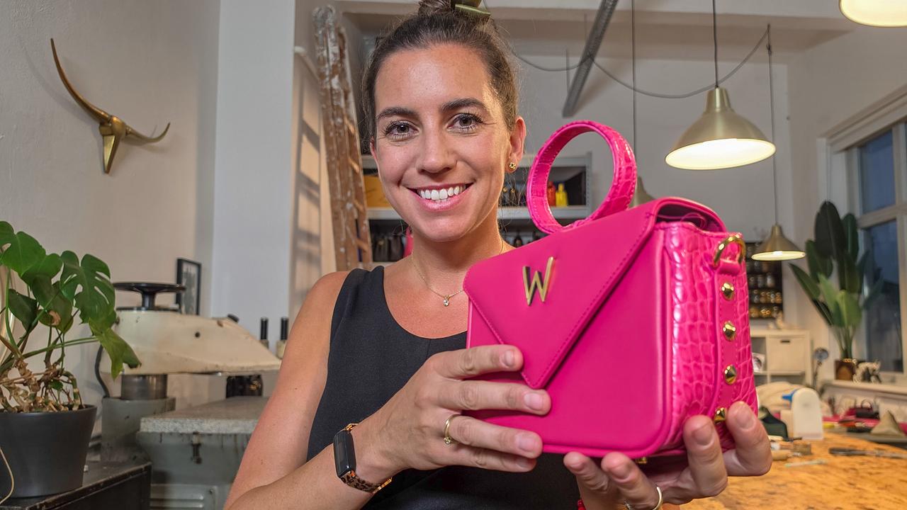 Katrin Motter hält in ihrer Werkstatt eine pinke Ledertasche mit goldfarbenem "W" und Nieten in den Händen.