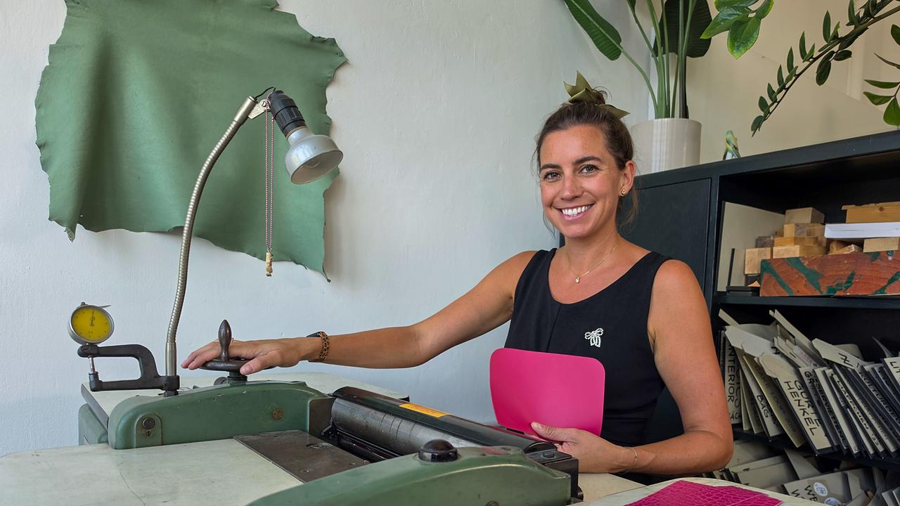 Katrin Motter sitzt lächelnd an einer grünen Ledermaschine und arbeitet an einer pinken Tasche.